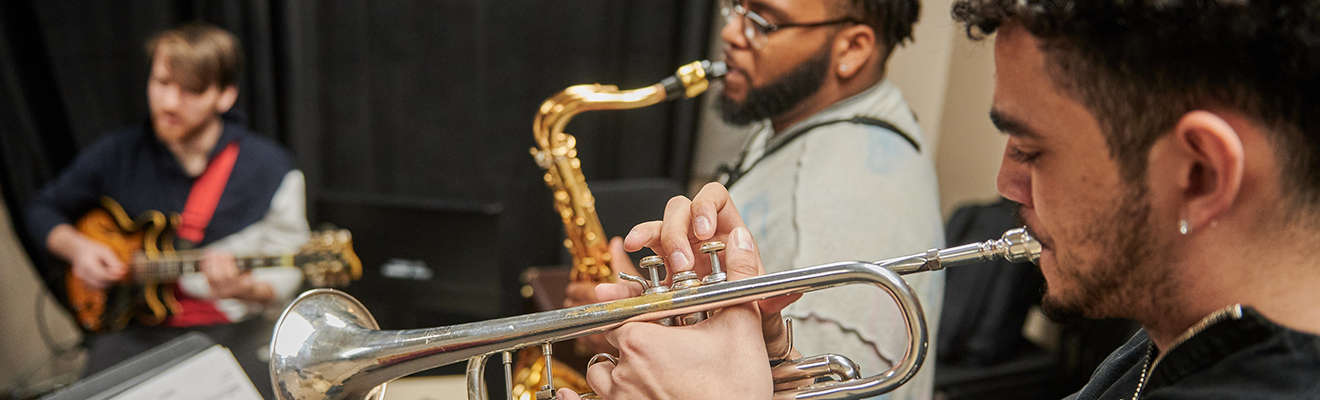 Three students play the guitar, saxophone, and trumpet.