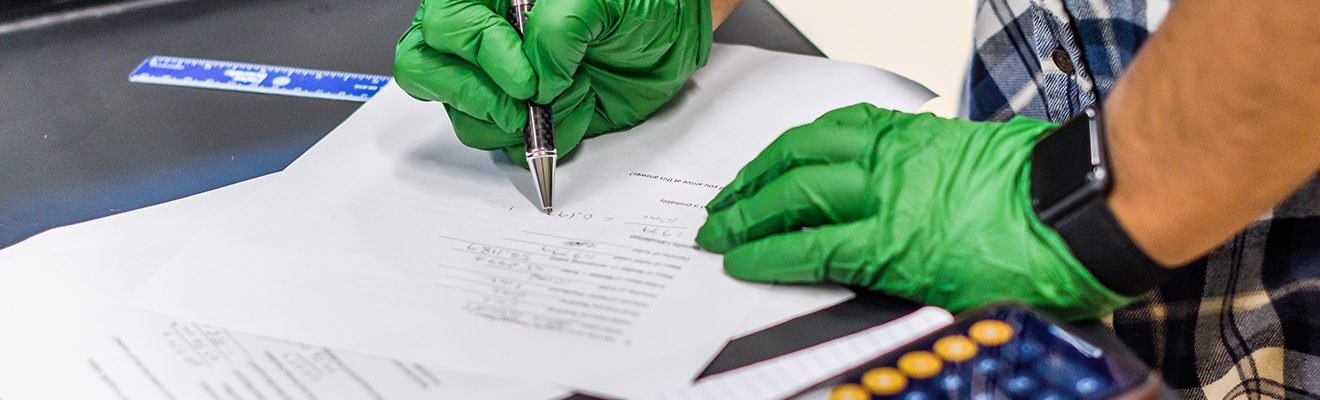hands with green gloves writing in a notebook