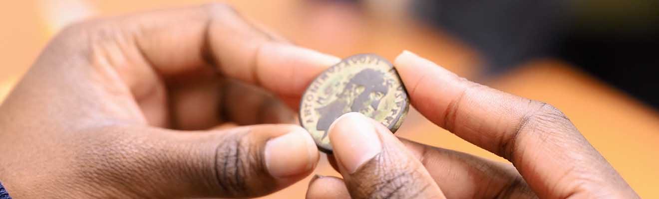 A set of hands carefully grasp an ancient coin