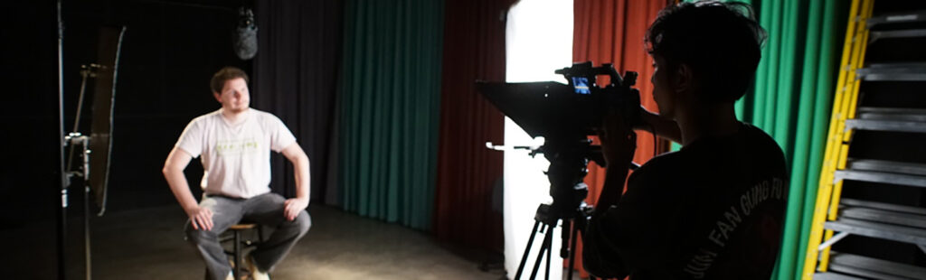 One student films another student sitting on a chair in Carmichael Studio.