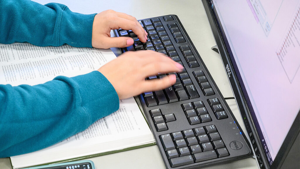 Student types her notes from a textbook into a computer.