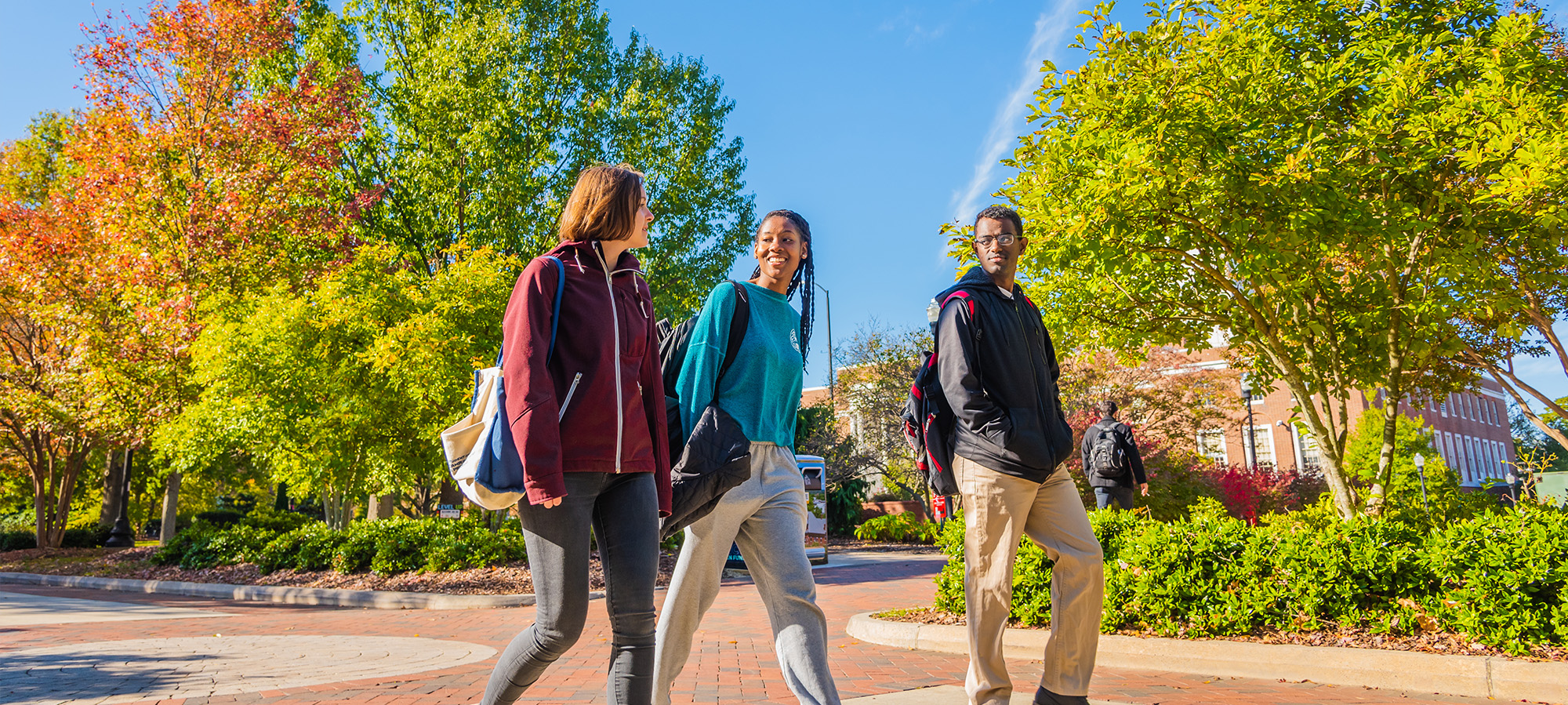 Students pass by trees that are beginning to change color in the fall.