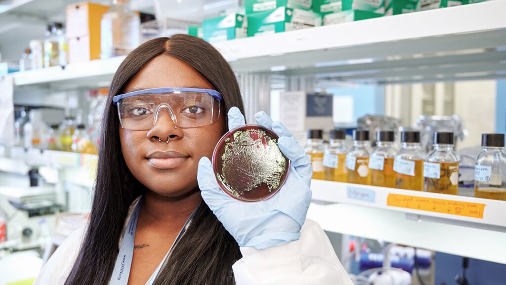 A woman in a laboratory holds up a petri dish.