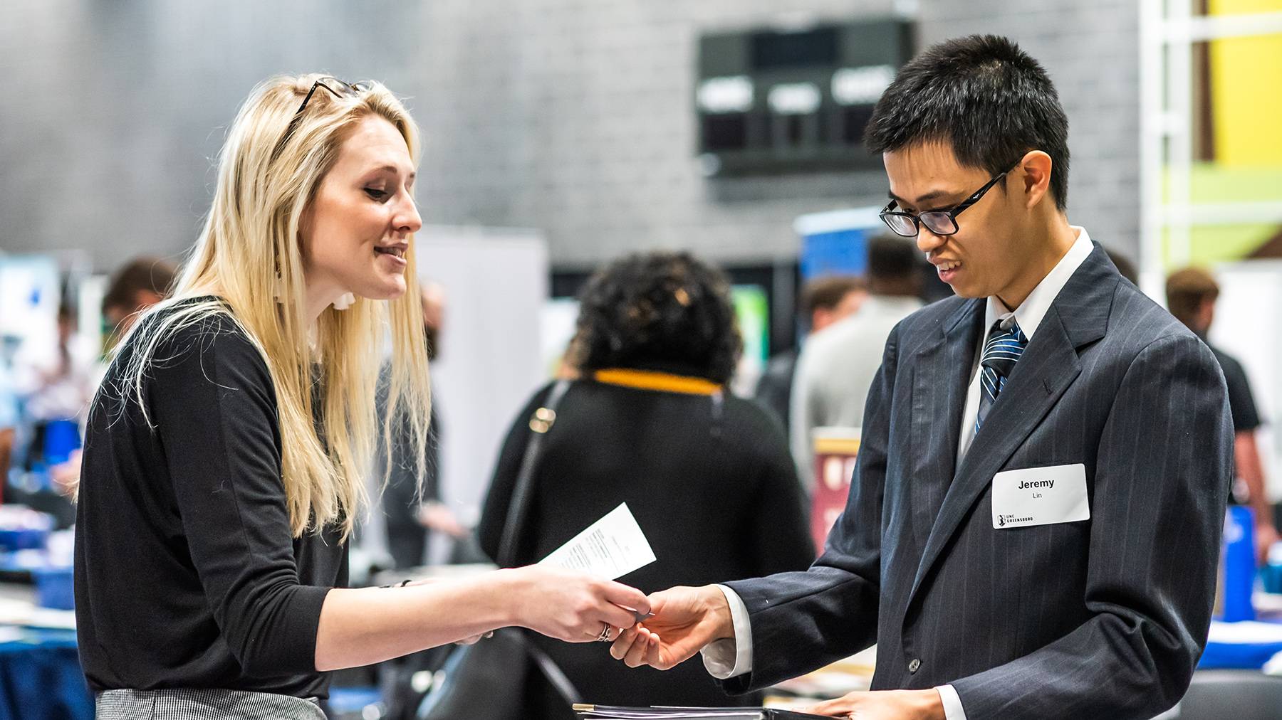 A student receives a business card from a hiring representative at an on-campus career fair.