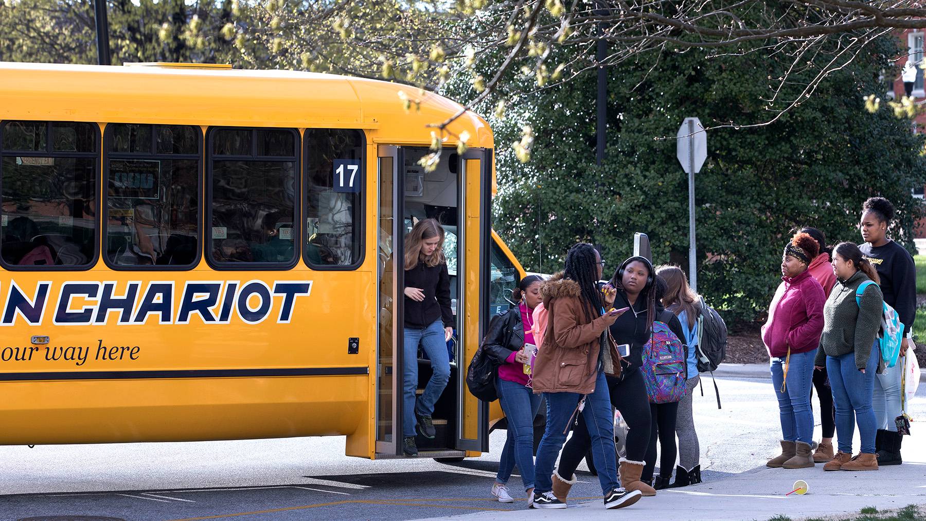 Students get off a Spartan Chariot at a bus stop while others wait to board.