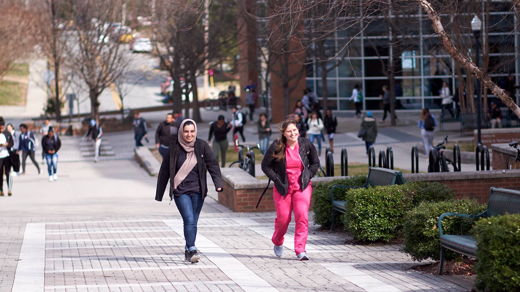 Two female students smile while walking away from the Nursing and Instructional Building.