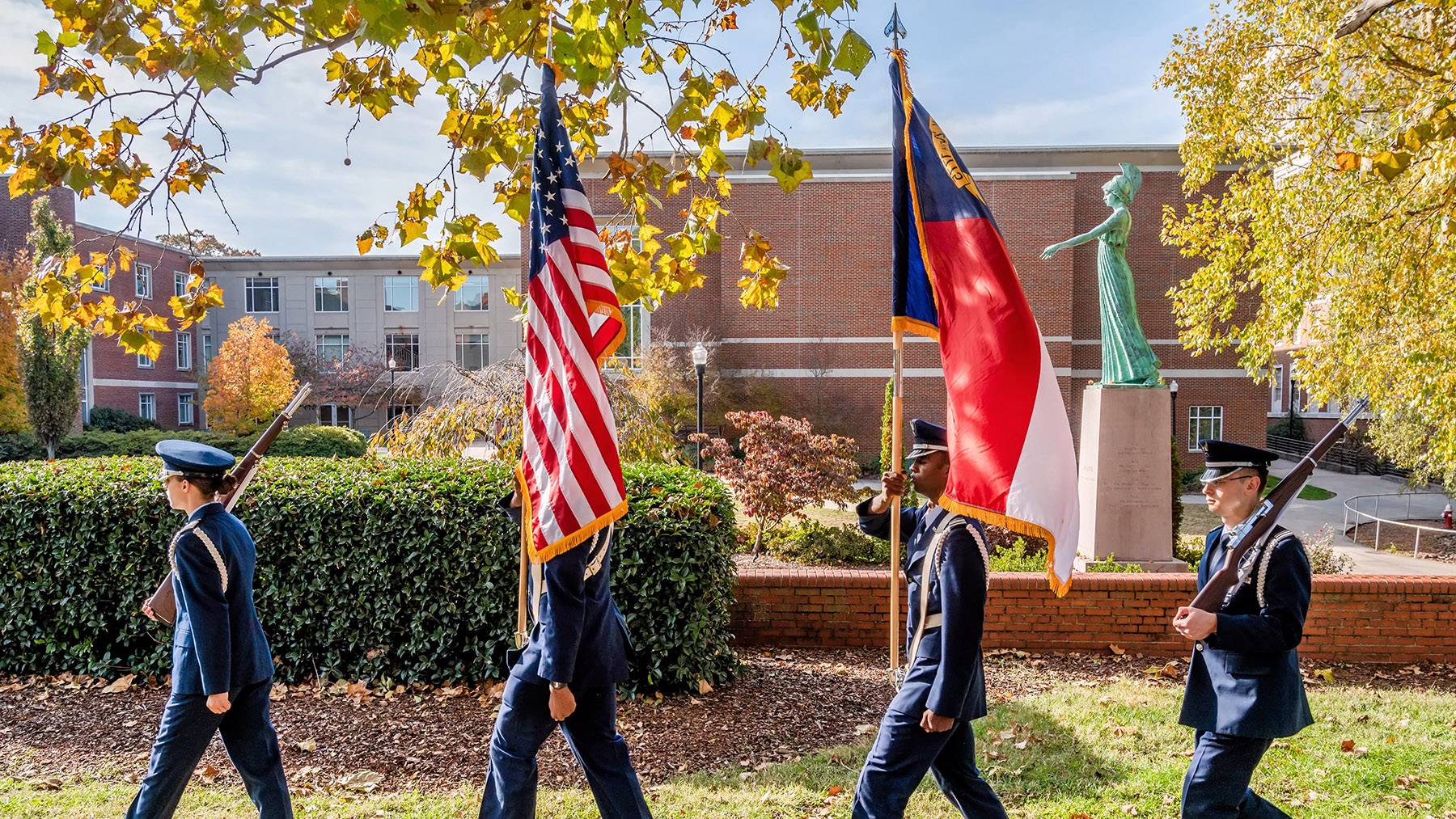 Air Force ROTC members march in formation with the US and North Carolina flags during a Veterans Day ceremony.