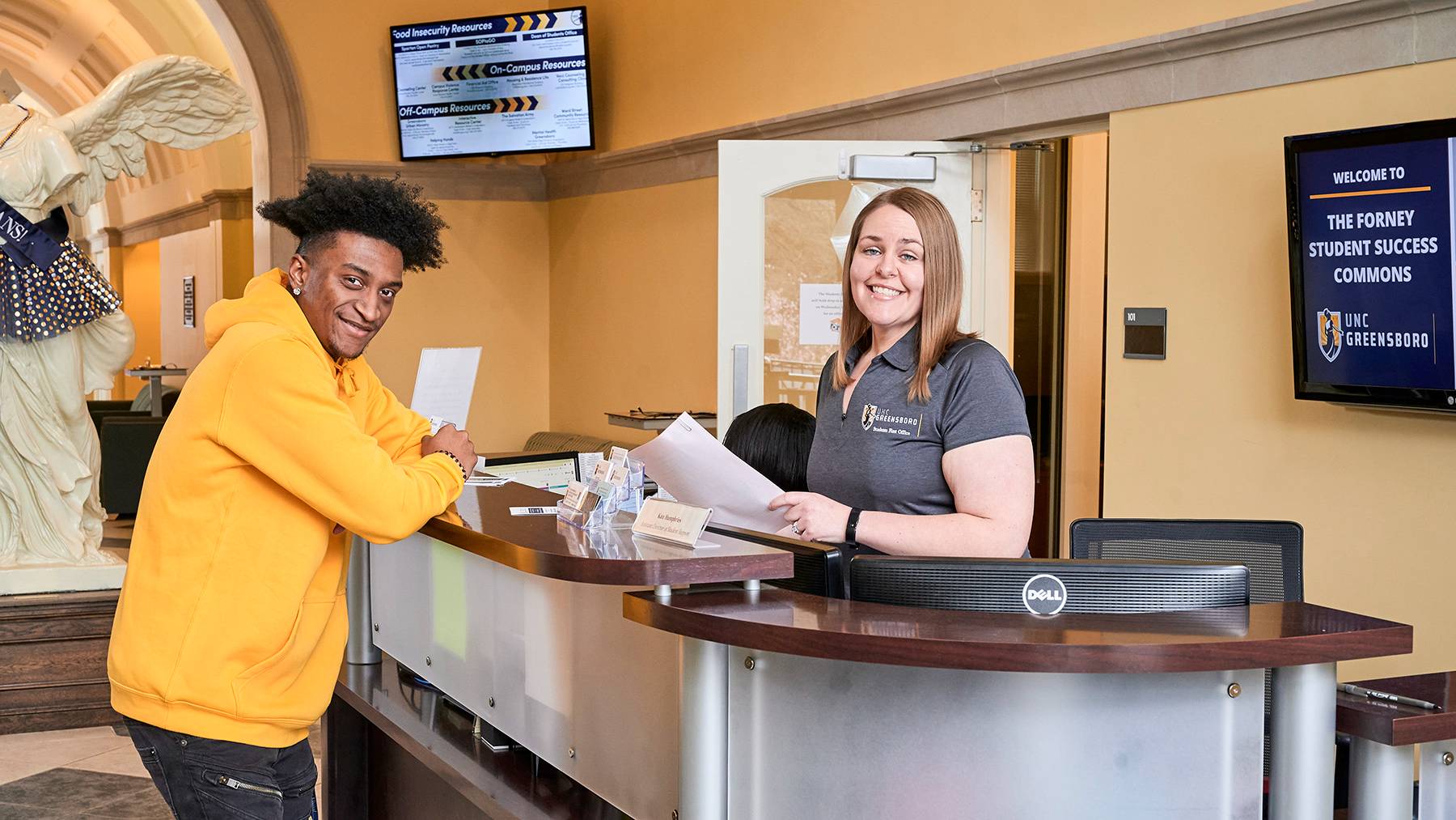 A student and employee pose for a picture together at the front desk of the Forney Student Success Commons.
