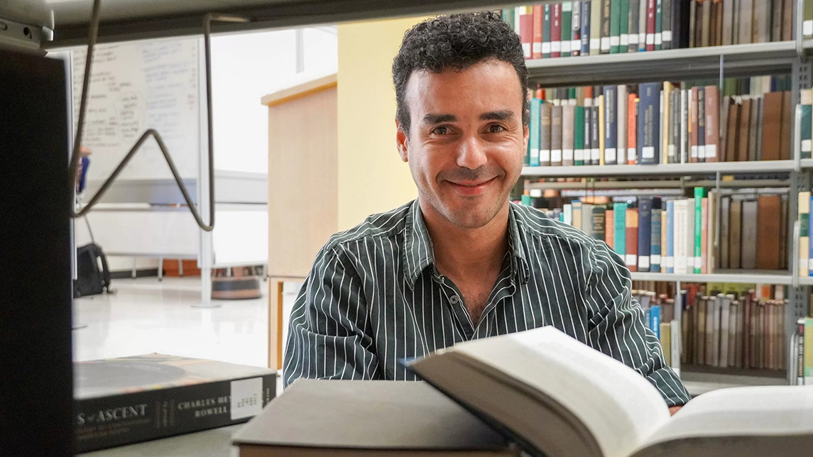 A man smiles at the camera with books behind him