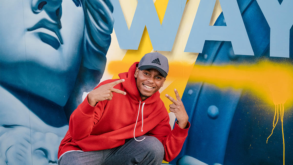 Student poses in front of a mural at the 2022 Homecoming.