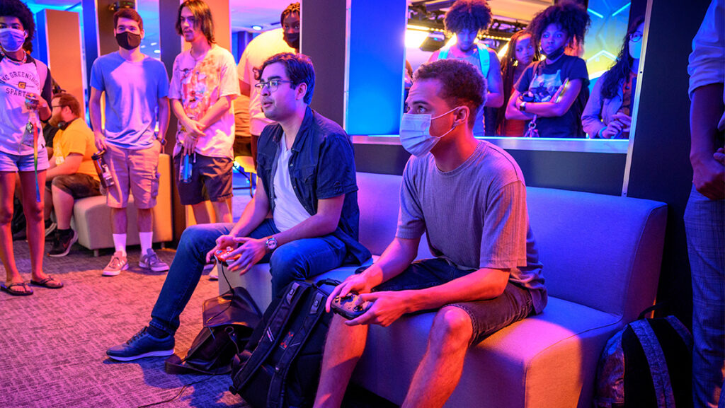 Two students with game controllers play against each other inside the Esports center.