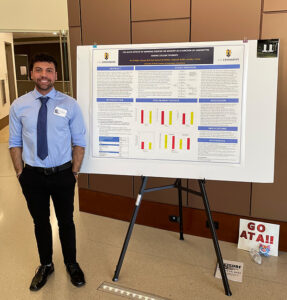 A man stands next to his research poster in professional clothing.