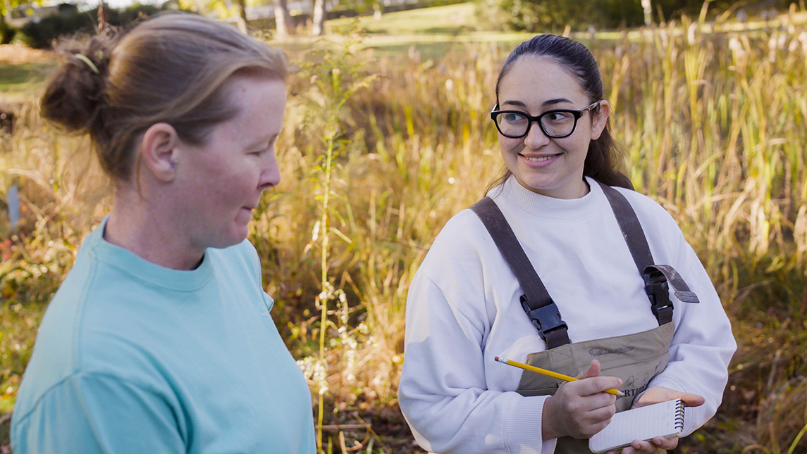 Two women chat in the wetlands, while one of the scientists writes notes in a notepad.
