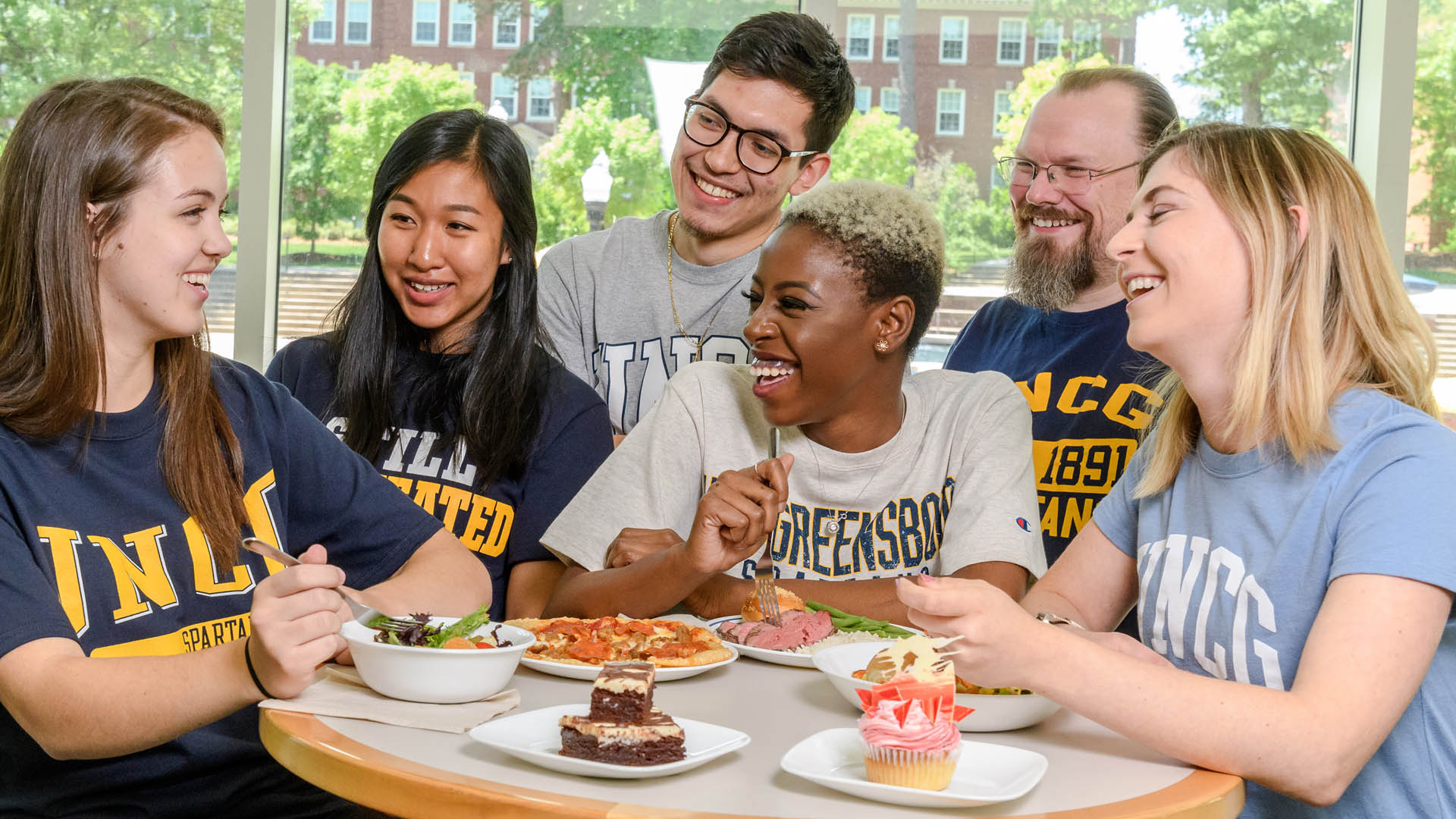 A diverse group of UNCG students laugh while eating at the Fountain View Dining Hall.