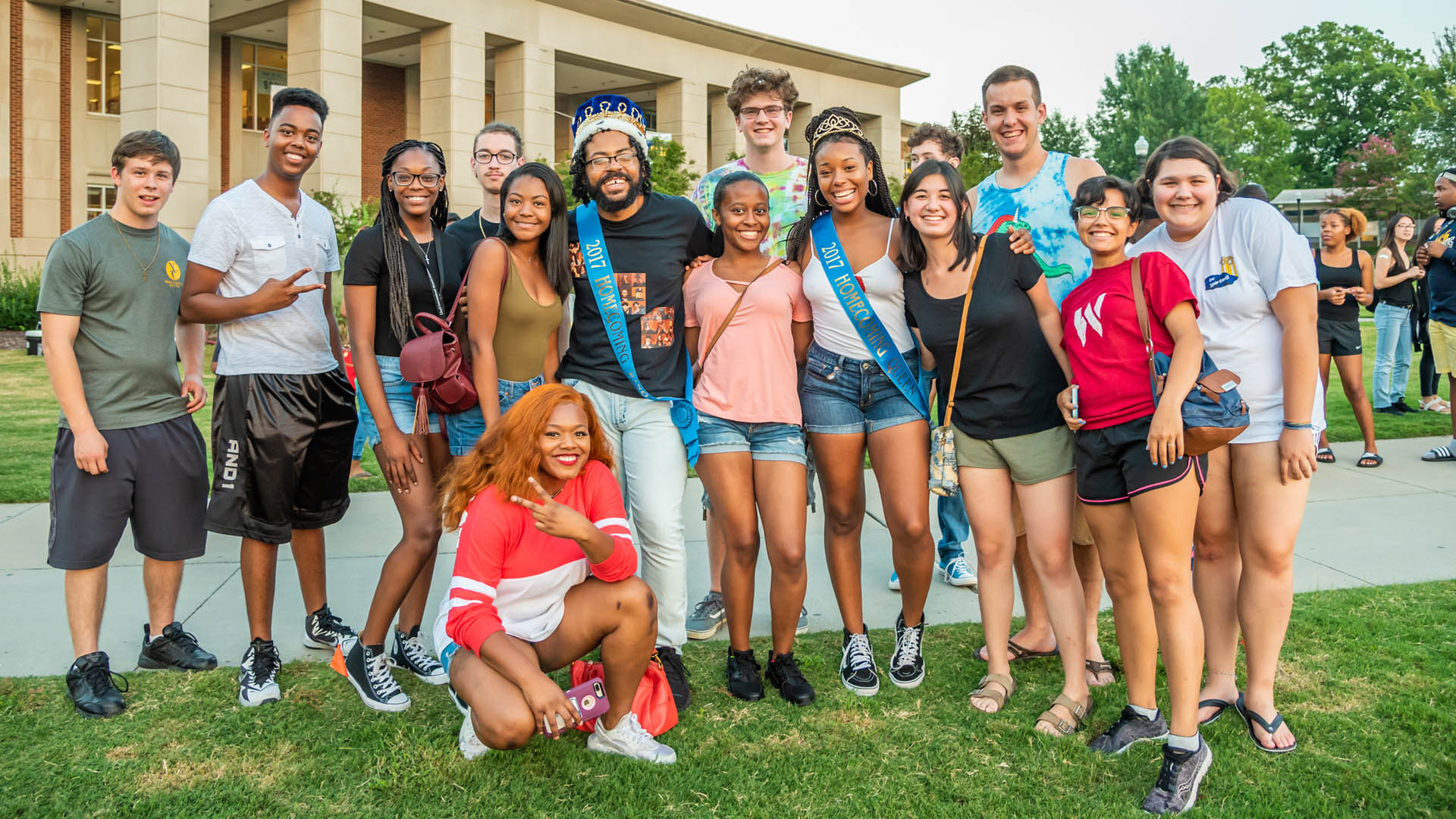 A diverse group of UNCG students pose for a picture on Kaplan Commons in front of the Elliott University Center.