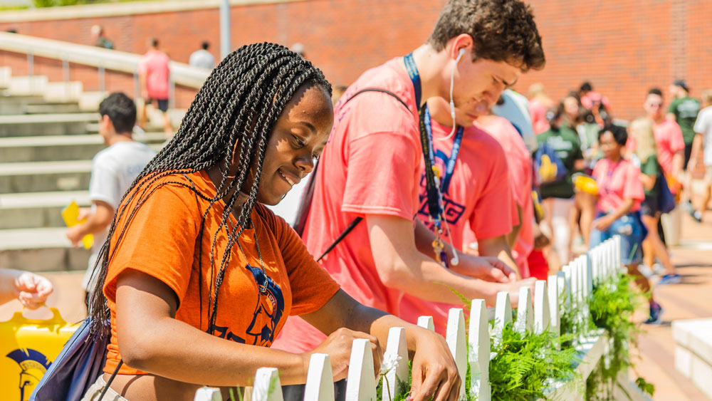 Students adding daisies to a fence during NAV1GATE student convocation.