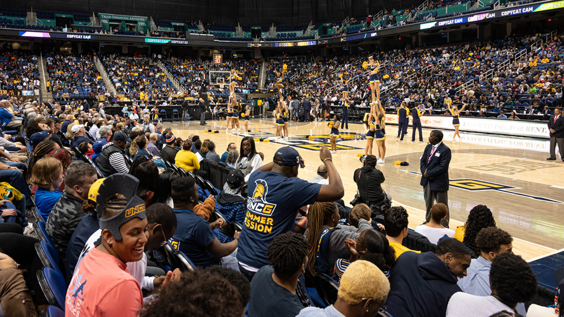 UNCG students clap while the cheerleading team performs on court during a men’s basketball game at the Greensboro Coliseum.