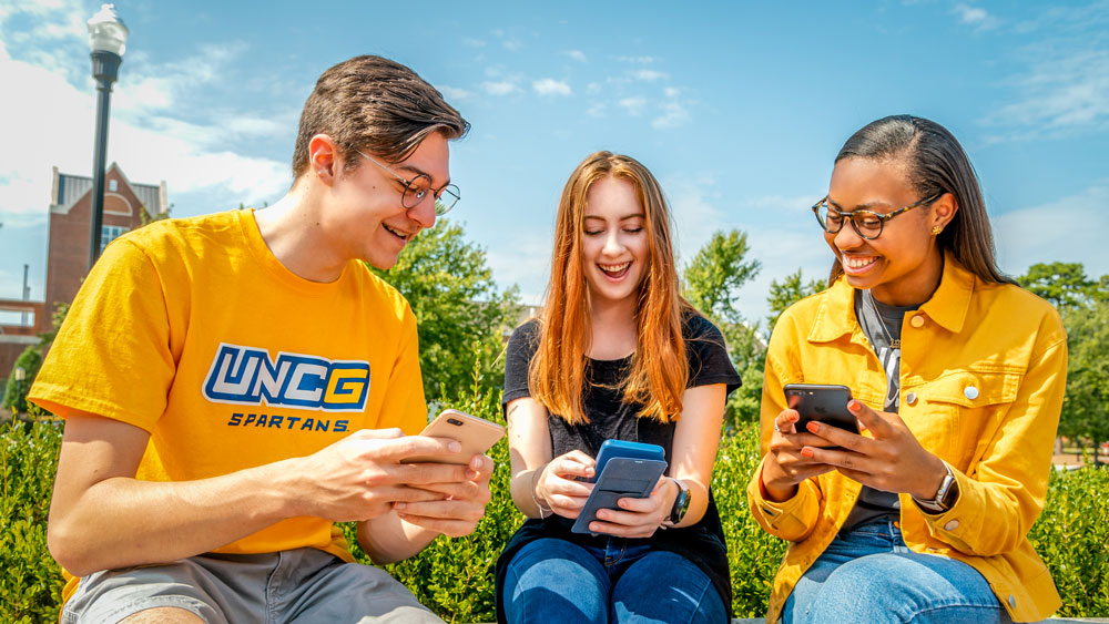 Three students looking and smiling at their cellphones