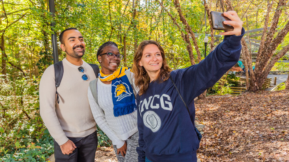 Three UNCG students, taking a moment to gather for a selfie on a sunny afternoon.