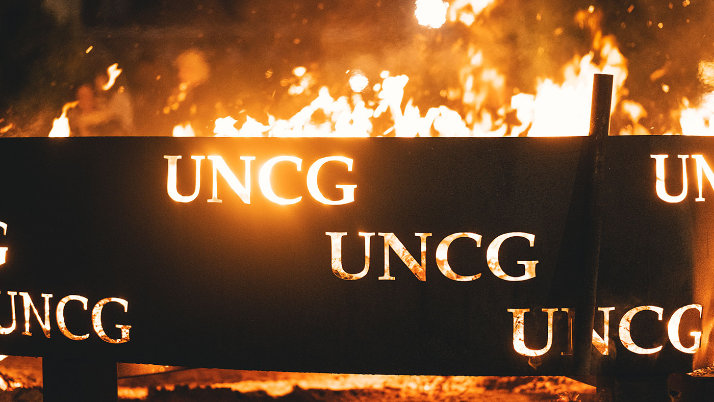 Alumni and current students gather around the annual UNCG Homecoming bonfire held on Moran Commons each fall.