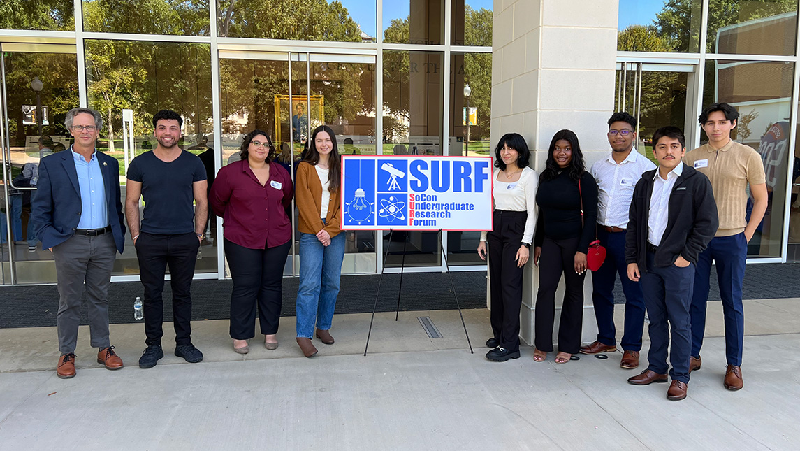 A group of undergraduate researchers stand with the director of undergraduate research outside of a building at a research conference