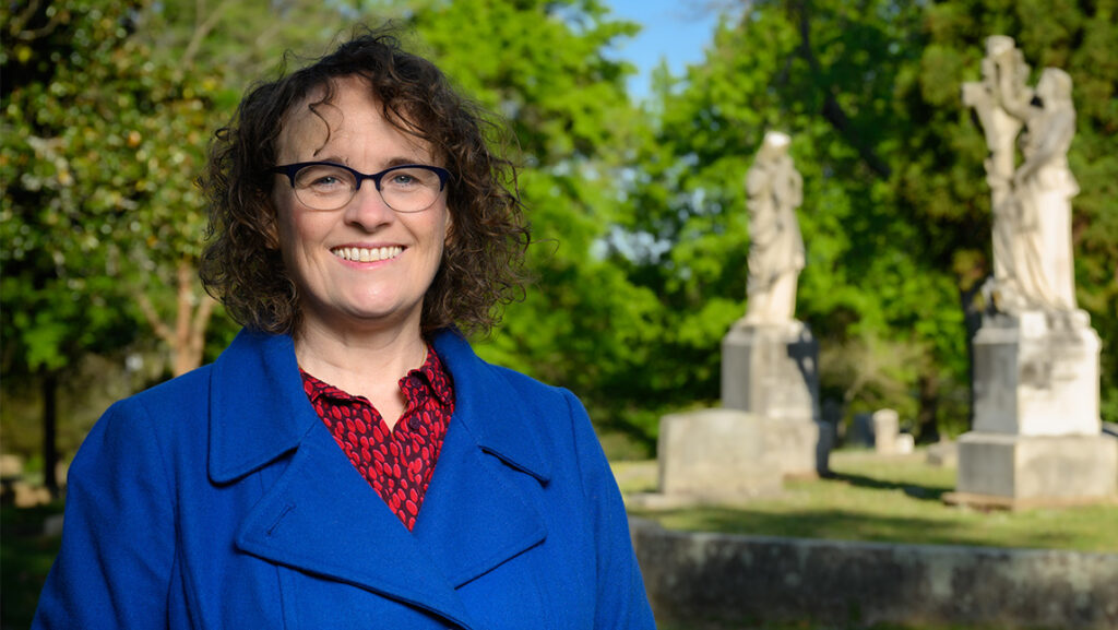 Dr. Joanne Murphy stands next to the statues in a cemetery.