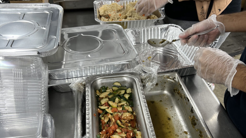 gloved hands scooping food into aluminum plates