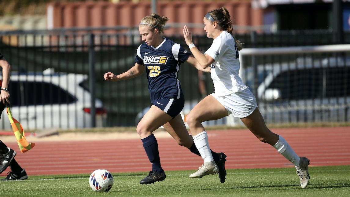 Maddy Gilhool running with an opponent on the UNCG soccer field
