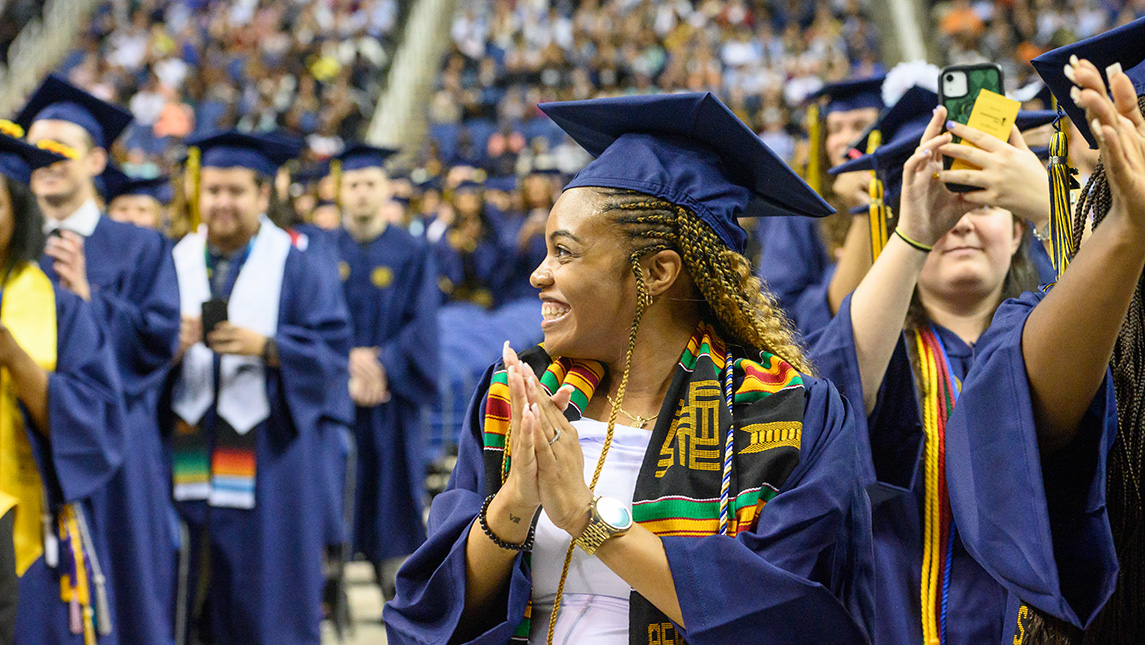 A woman in her cap and gown claps at graduation.