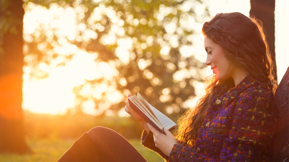 Female student studying in a park at sunset.