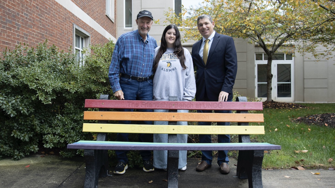Claire Corrigan, Dr. Stuart Schleien and UNCG faculty member stand together behind the rainbow colored friendship bench.