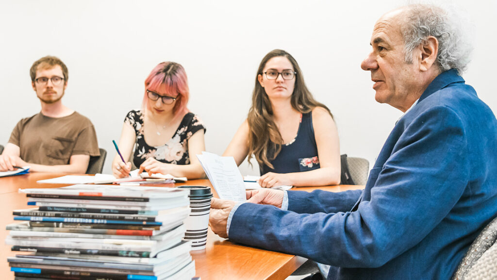Professor Stuart Dischell talks to writing students with pen, paper, and a stack of books.