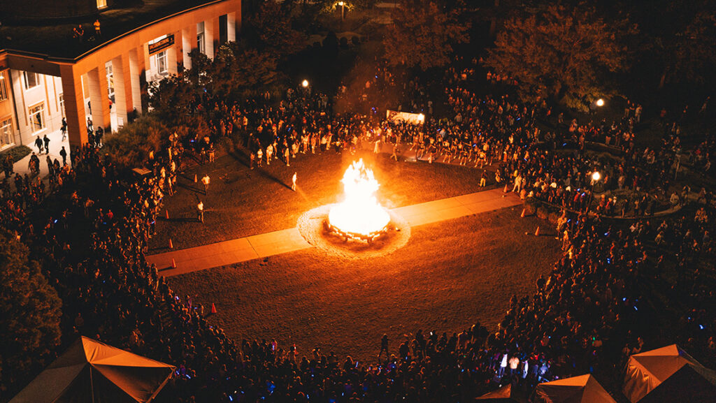 Crows of students gather around Homecoming 2022 bonfire at night.