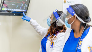 Two nursing students study a health vitals monitor.
