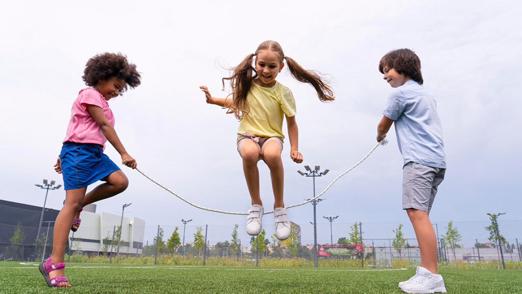 Three children jump rope on a playground.
