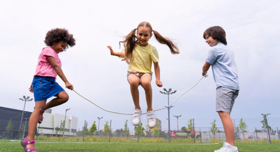 Three children jump rope on a playground.