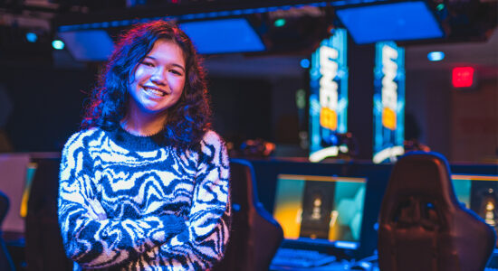 Student Jordin Hipps poses in the esports arena with gaming consoles in the background.