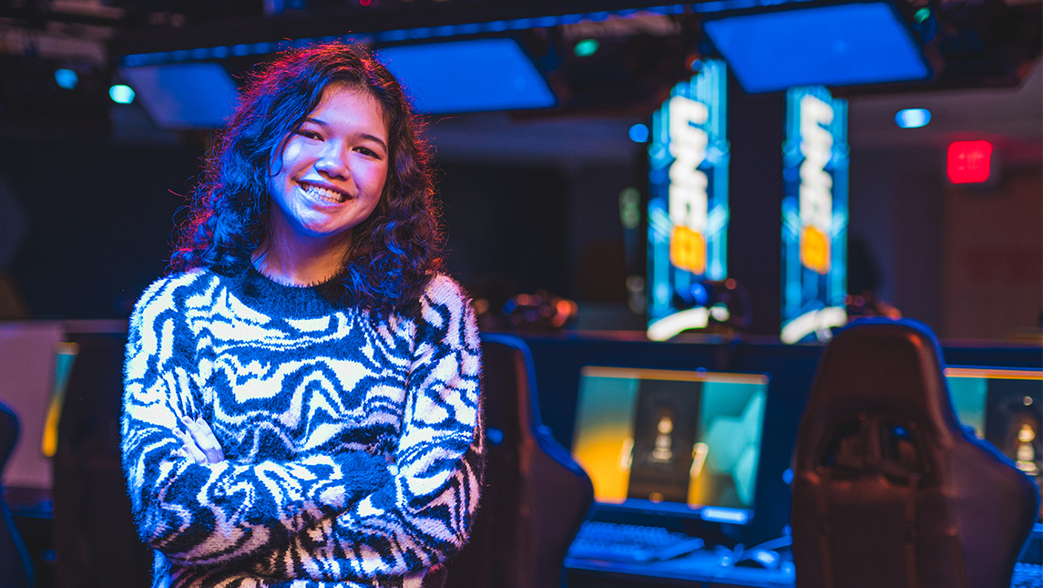 Student Jordin Hipps poses in the esports arena with gaming consoles in the background.