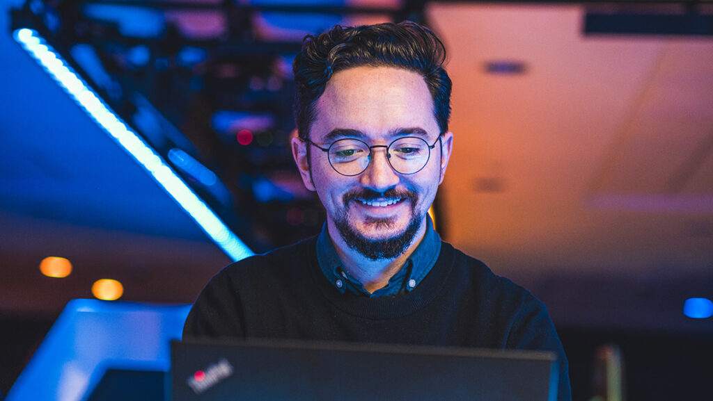 A man smiles while working on his computer in the Esports Arena.