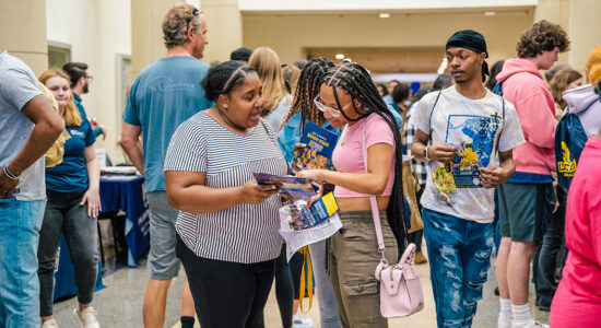A prospective student and her mom look at brochures in a crowded hall during orientation.