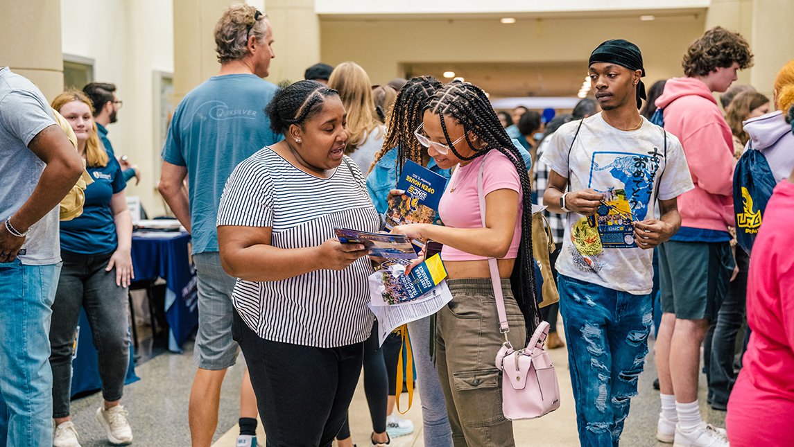 A prospective student and her mom look at brochures in a crowded hall during orientation.