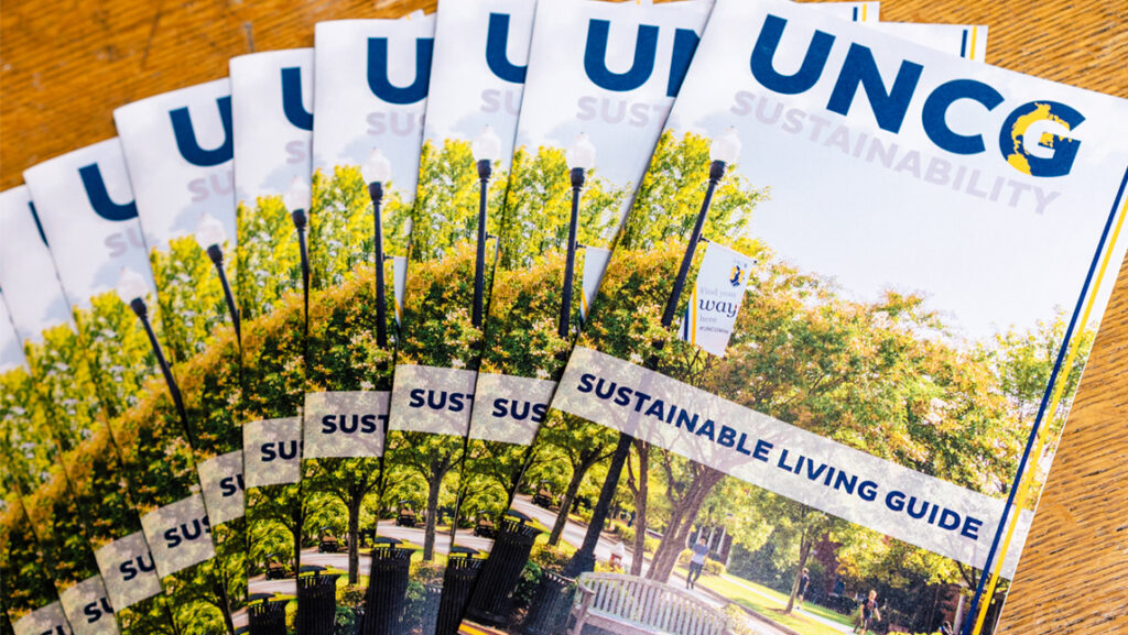 Several copies of the UNCG Sustainability Living guide laid out on a table