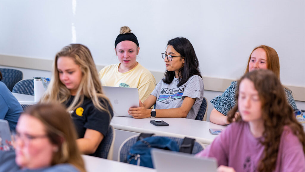 Students sitting in a classroom look at notes on a laptop.