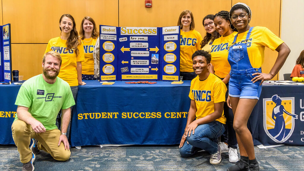 Students wearing UNCG t-shirts gather around the Student Success booth at the majors and minors career fair.