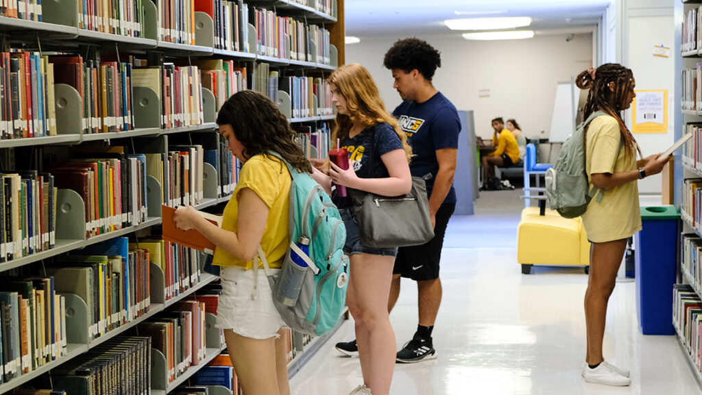 4 Students look at books they pulled off the library shelves.