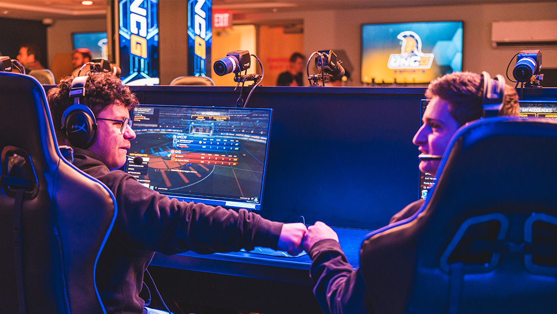 Two gamers fist bump as they play Rocket League in the UNCG esports arena.