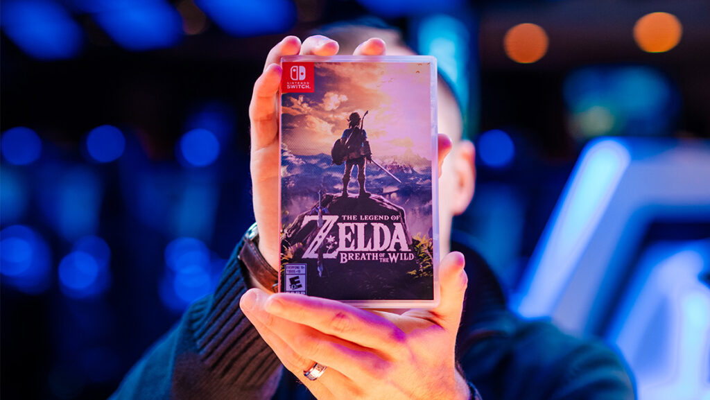 A person holds up the case for "The Legend of Zelda: Breath of the Wild."
