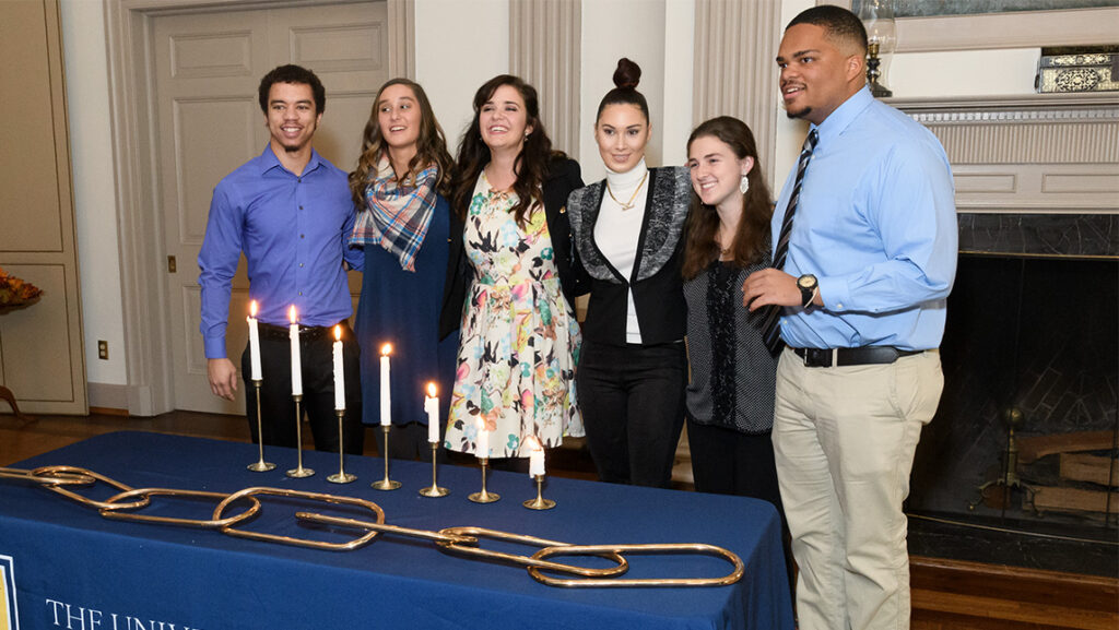 Inductees to the Golden Chain Society in 2017 gather around the table with the golden chain and candles.