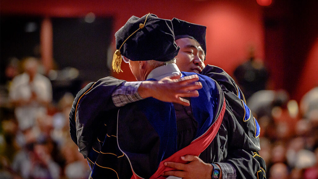 Graduate student hugs a professor at doctoral hooding ceremony.