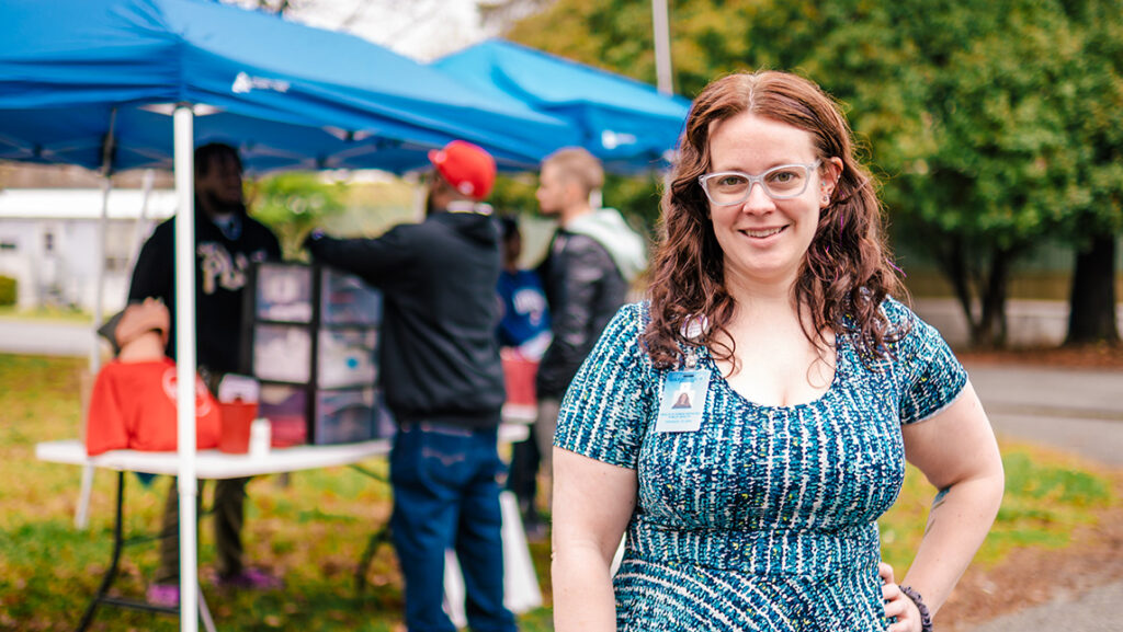 Woman with badge stands in front of a tent covering a table with medical supplies.